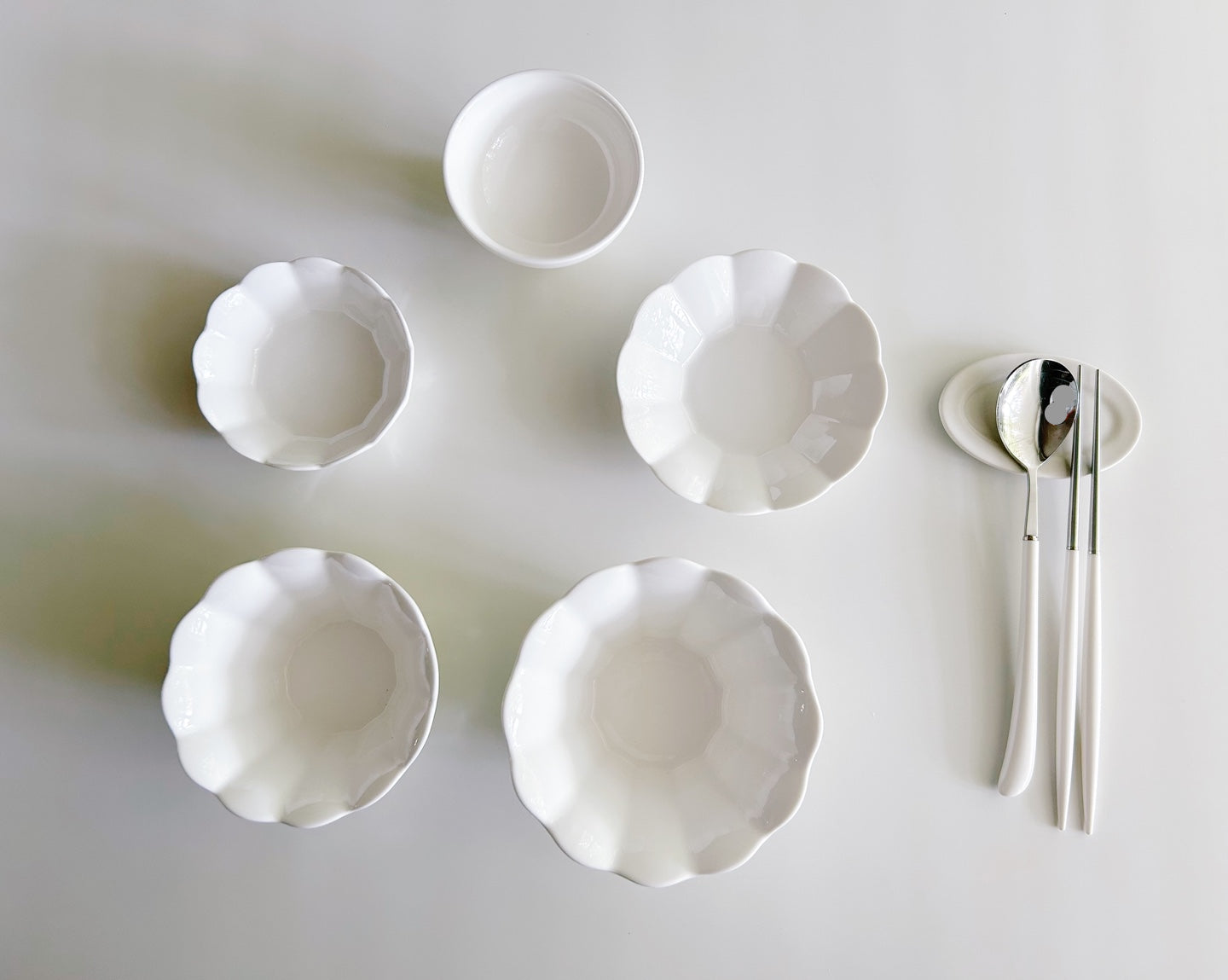 Set of white ceramic bowls and silver cutlery on a light gray background