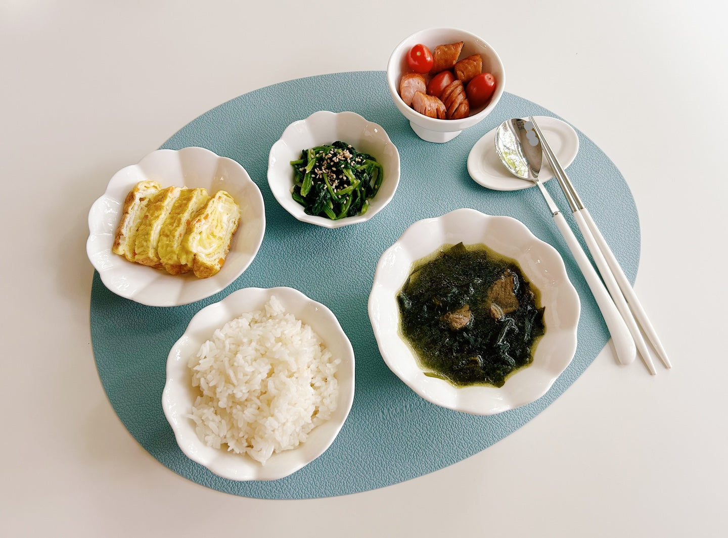 Assorted Korean dishes including rice, pickled vegetables, and kimchi on a blue placemat.