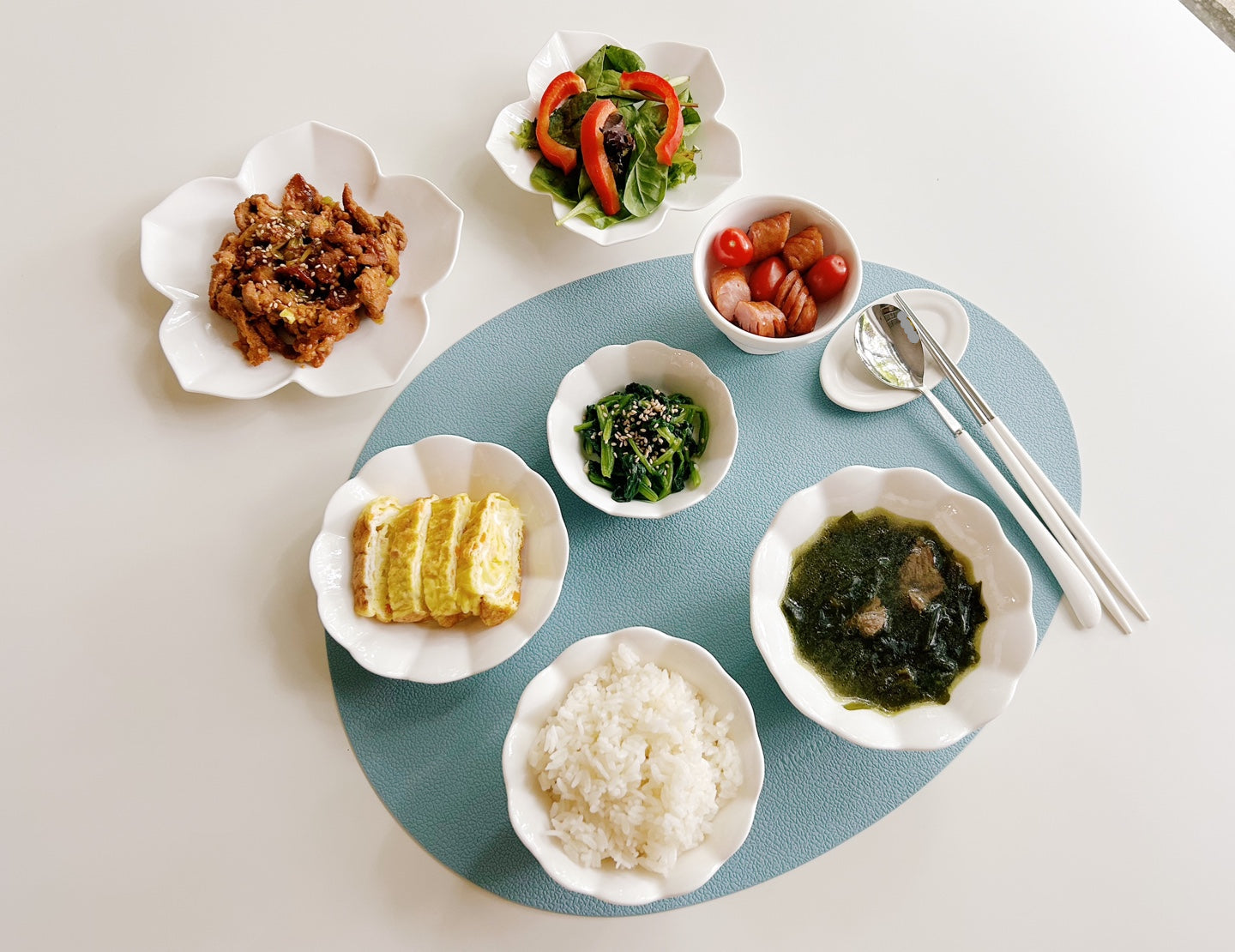 Assorted dishes of food on a round blue placemat with cutlery on a light gray background