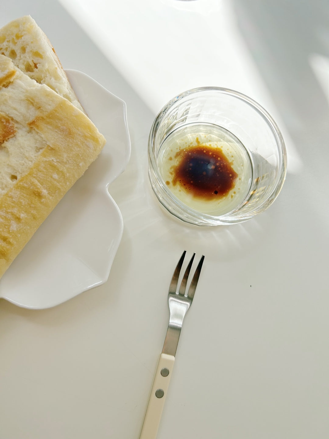 Glass dish with a dark brown substance, a fork, and bread on a white surface