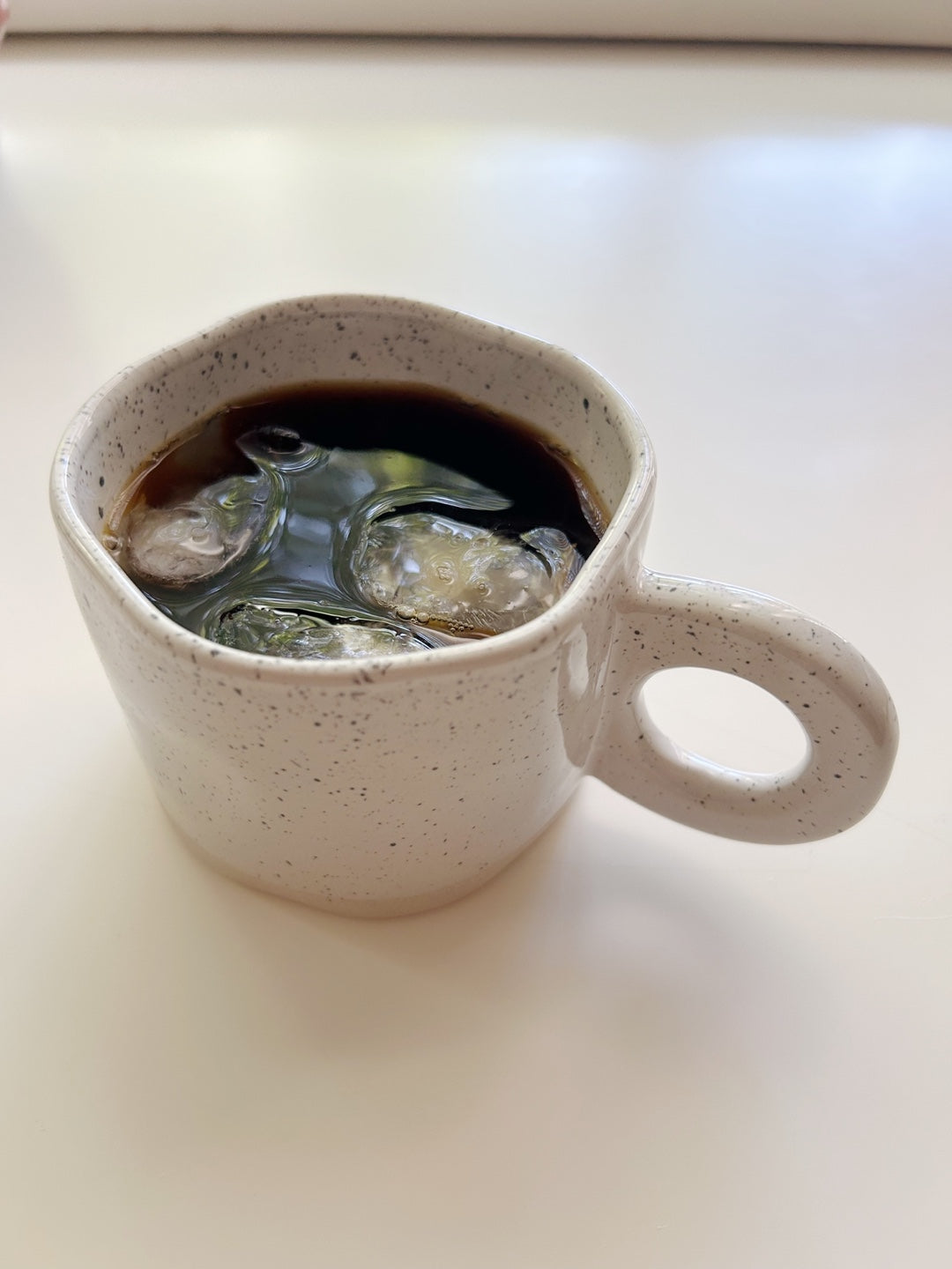 White ceramic mug with a handle filled with dark liquid on a white surface
