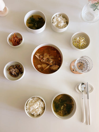 Assorted Korean dishes including soup, rice, and side dishes on a white table.